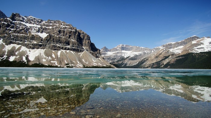 Snow-capped mountains reflected in a partially frozen lake