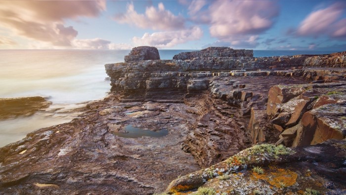 Rocky coast with ocean waves and clouds at sunset