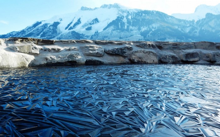 Frozen lake with snow-capped mountains and stone wall