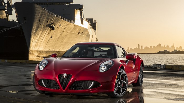 Red Alfa Romeo 4C parked by a ship and city skyline