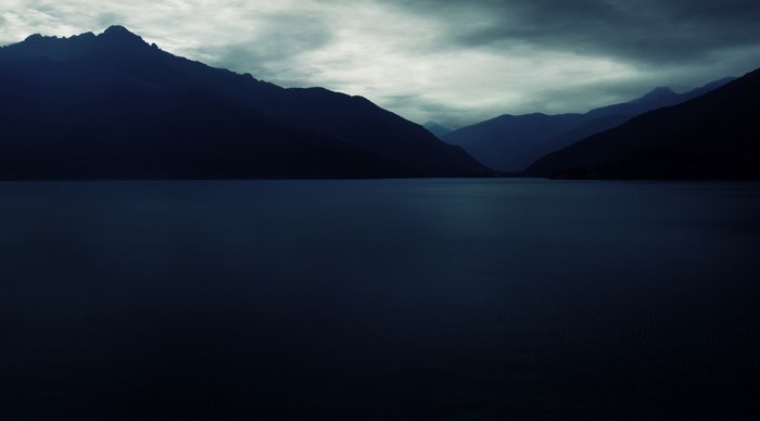 Dark mountains over a still lake at dawn