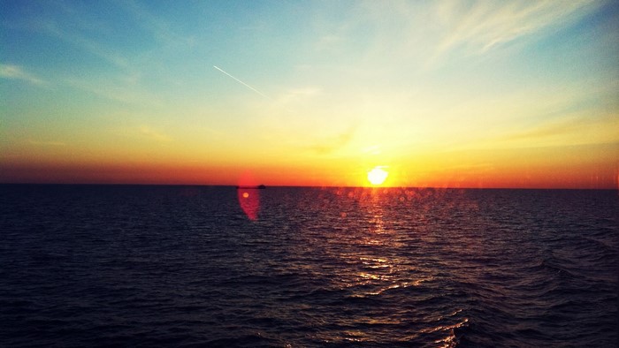 Sunset over the ocean with a ship and contrail