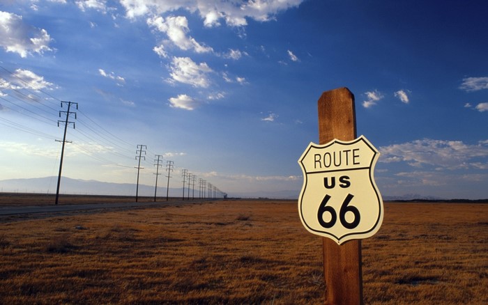 Route 66 sign in a dry field with power lines