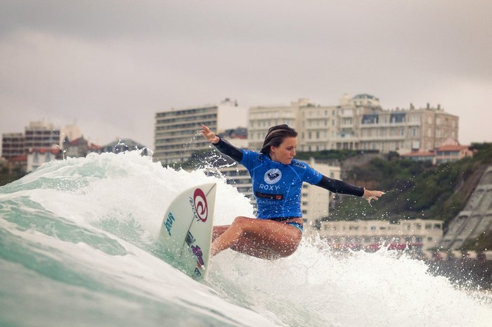 Woman surfing a wave with buildings in the background