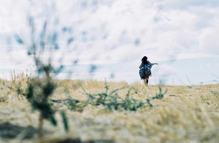 Woman in poncho walking in a dry grassy landscape