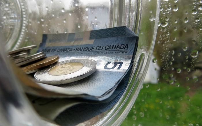 Canadian five dollar bill and coins in a jar