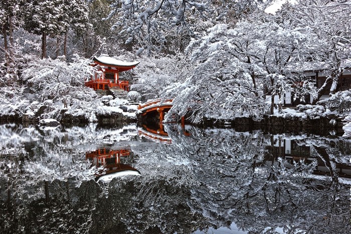 Japanese pagoda and bridge reflected in water during winter snow