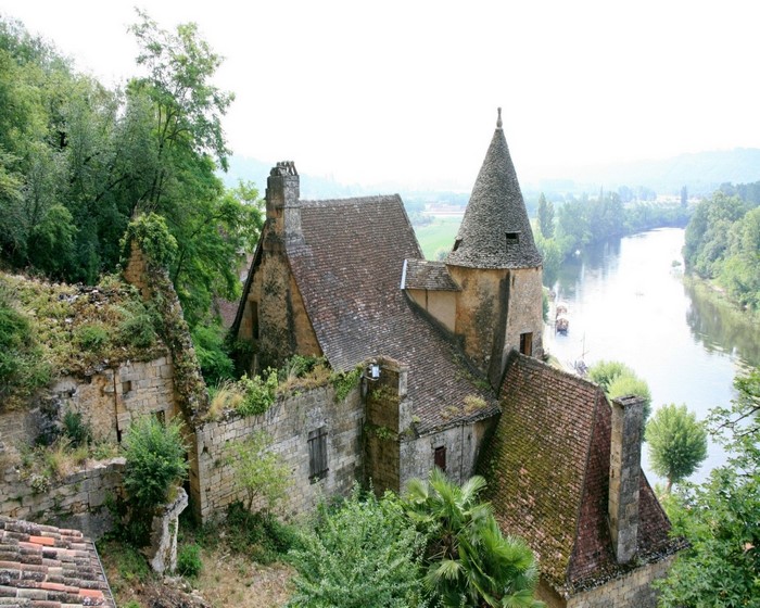 Overgrown stone buildings and tower by a river