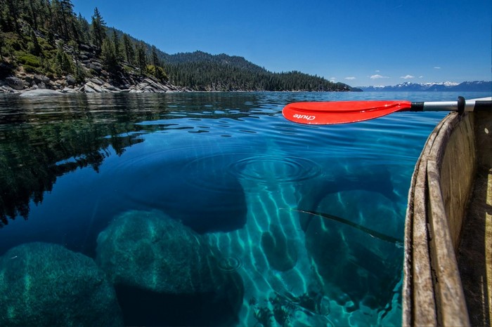 Canoe paddle in clear blue lake water with submerged rocks