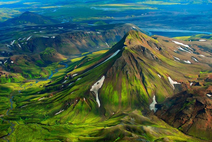 Aerial view of a green mountainous valley in Iceland with snow patches