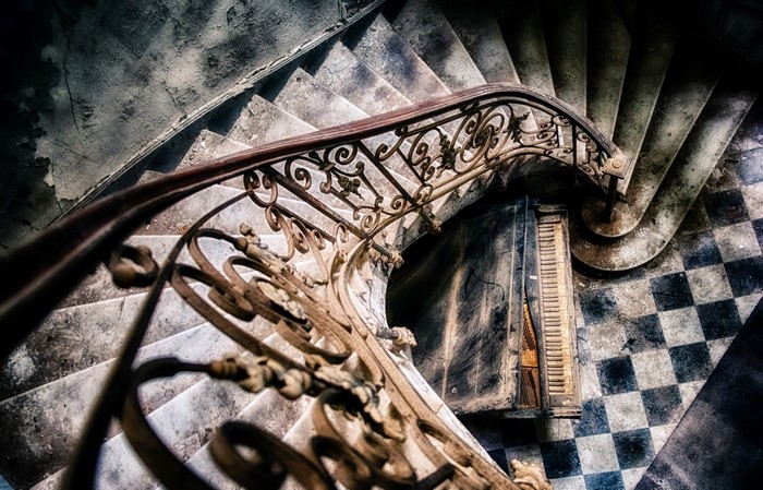 Old spiral staircase with ornate iron railing and checkered floor