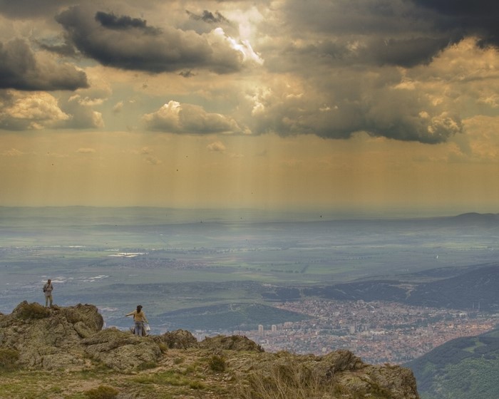Two people on a rocky outcrop overlooking a city and valley