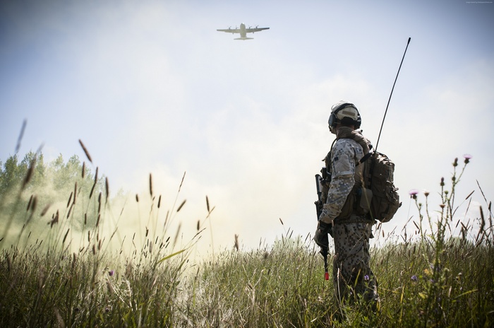 Soldier in a field watches an aircraft fly overhead