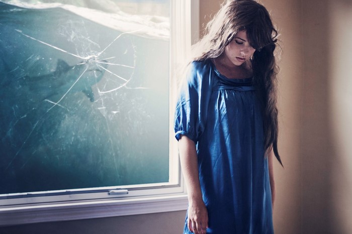 Woman in blue dress looking down with shark outside window