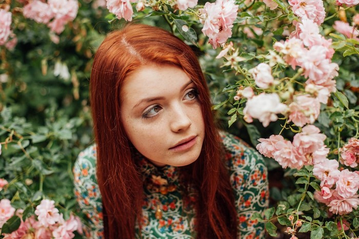 Redhead woman with freckles in a floral dress surrounded by pink roses