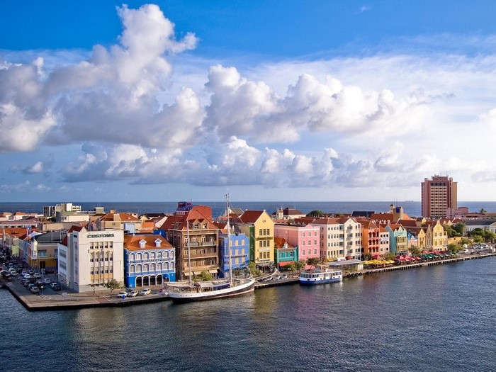 Colorful buildings along a harbor with boats and a tall building in the distance