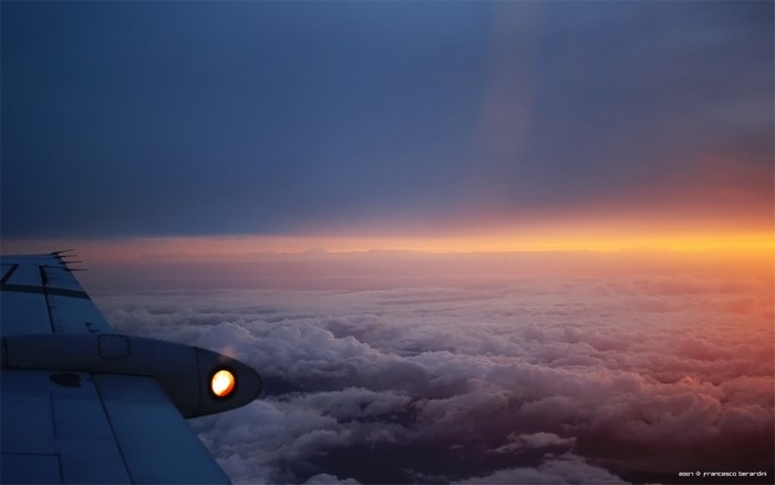 Airplane wing and engine light over clouds at sunset