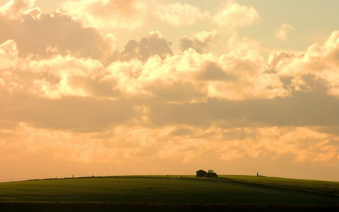Tractor on a grassy hill under a cloudy sky