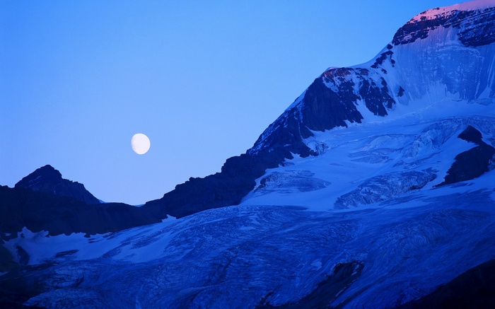 Moon over a snow-covered mountain range at dusk