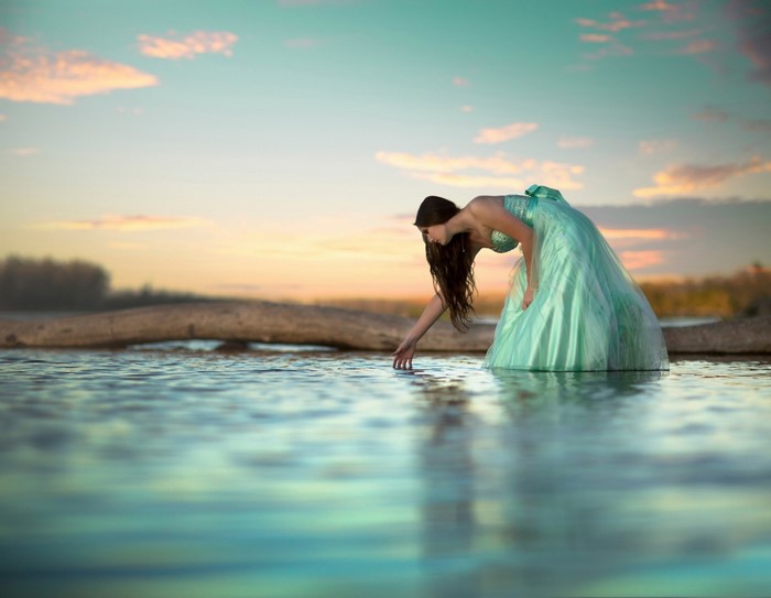 Woman in a dress touching water at sunset
