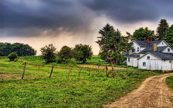 Farmhouse with dirt road and stormy sky