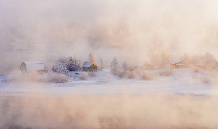 Winter morning mist over a snowy village by the water