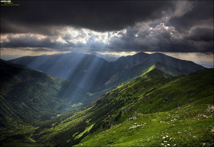 Sunlight beams through clouds over a green mountain valley