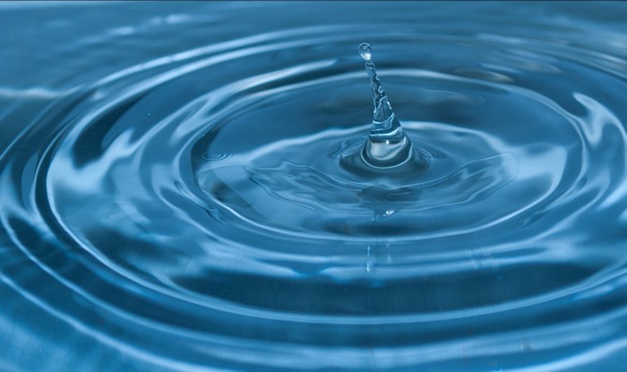Water drop creating ripples on blue surface