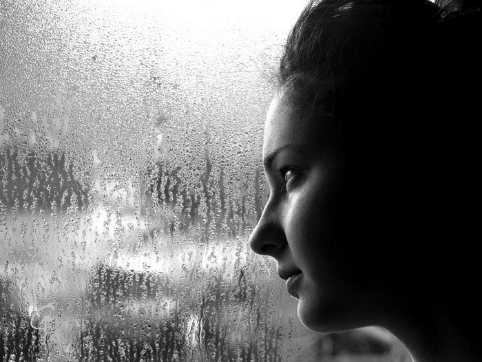 Woman looking out a rain-streaked window