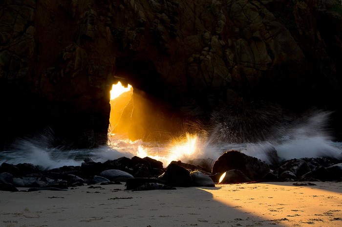 Sunlight shining through a sea cave onto a rocky beach