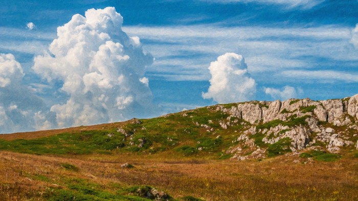 Cumulus clouds over a grassy hill with rocky outcrops