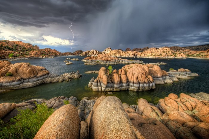 Lightning strikes over a rocky lake landscape