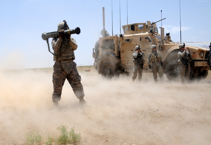Soldier fires rocket launcher near armored vehicle in desert