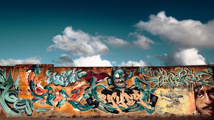 Graffiti mural on a wall with a blue sky and clouds