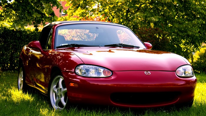 Red Mazda MX-5 Miata convertible parked on grass