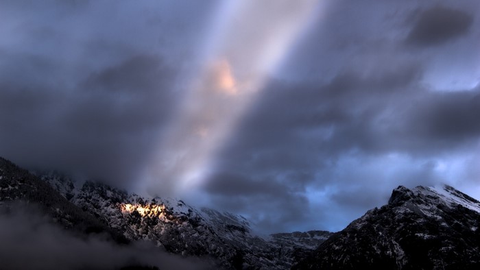Sunbeam illuminates snowy mountains under cloudy sky