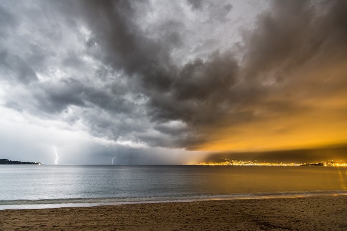 Lightning storm over the sea at dusk with city lights