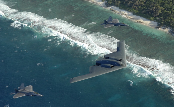 B-2 Spirit and F-22 Raptors fly over the ocean