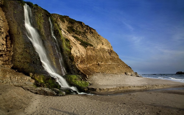 Waterfall cascading down a cliff onto a sandy beach