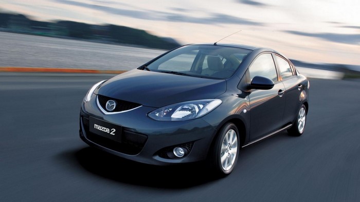 Dark blue Mazda 2 sedan driving on a road
