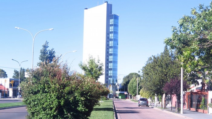 Modern glass tower building on a city street with trees