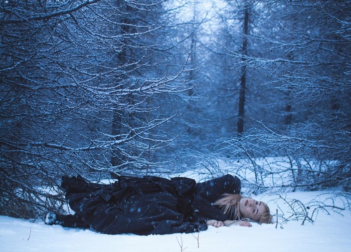 Woman in black dress lying in snowy forest