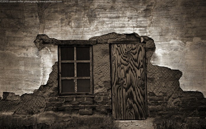 Monochrome photograph of a dilapidated wall with a window and door