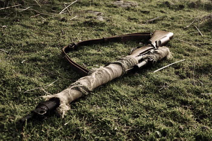 Sniper rifle wrapped in camouflage on grass