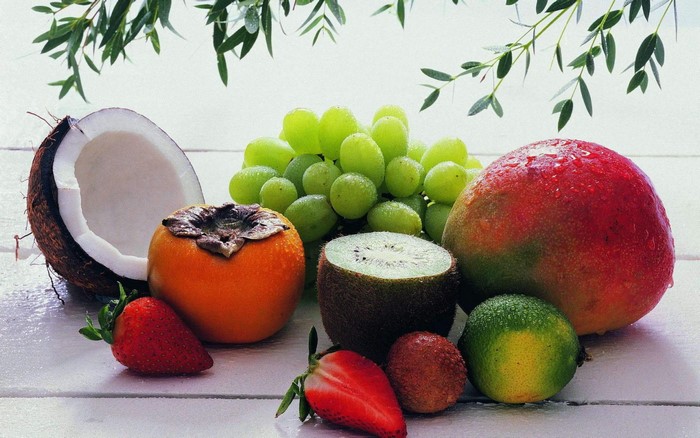Still life of various fruits including coconut, persimmon, kiwi, mango, grapes, strawberries, lychee, and lime
