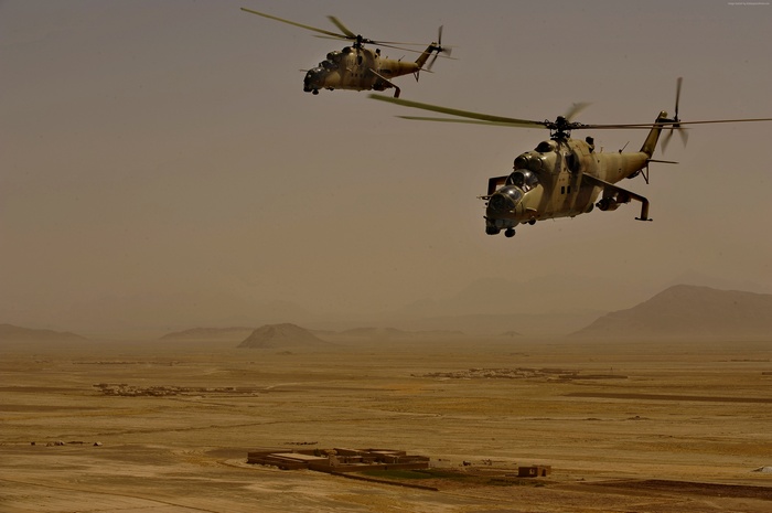 Two Mil Mi-35 attack helicopters flying over a desert landscape