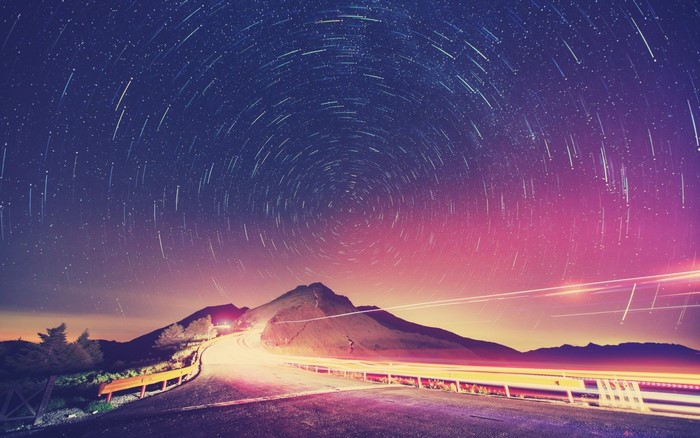 Star trails over a mountain road at night