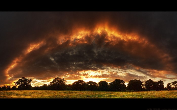 Fiery clouds over a grassy field at sunset