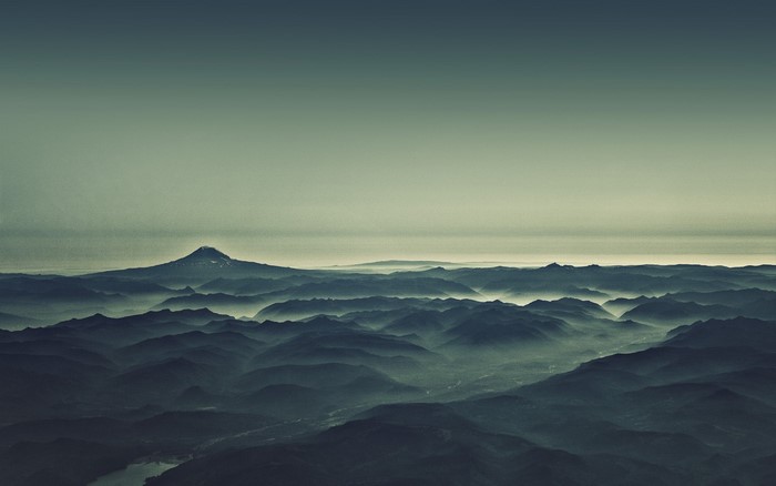 Misty mountains and a distant volcano under a hazy sky