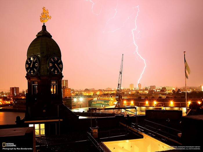 Clock tower with ship weather vane during lightning storm